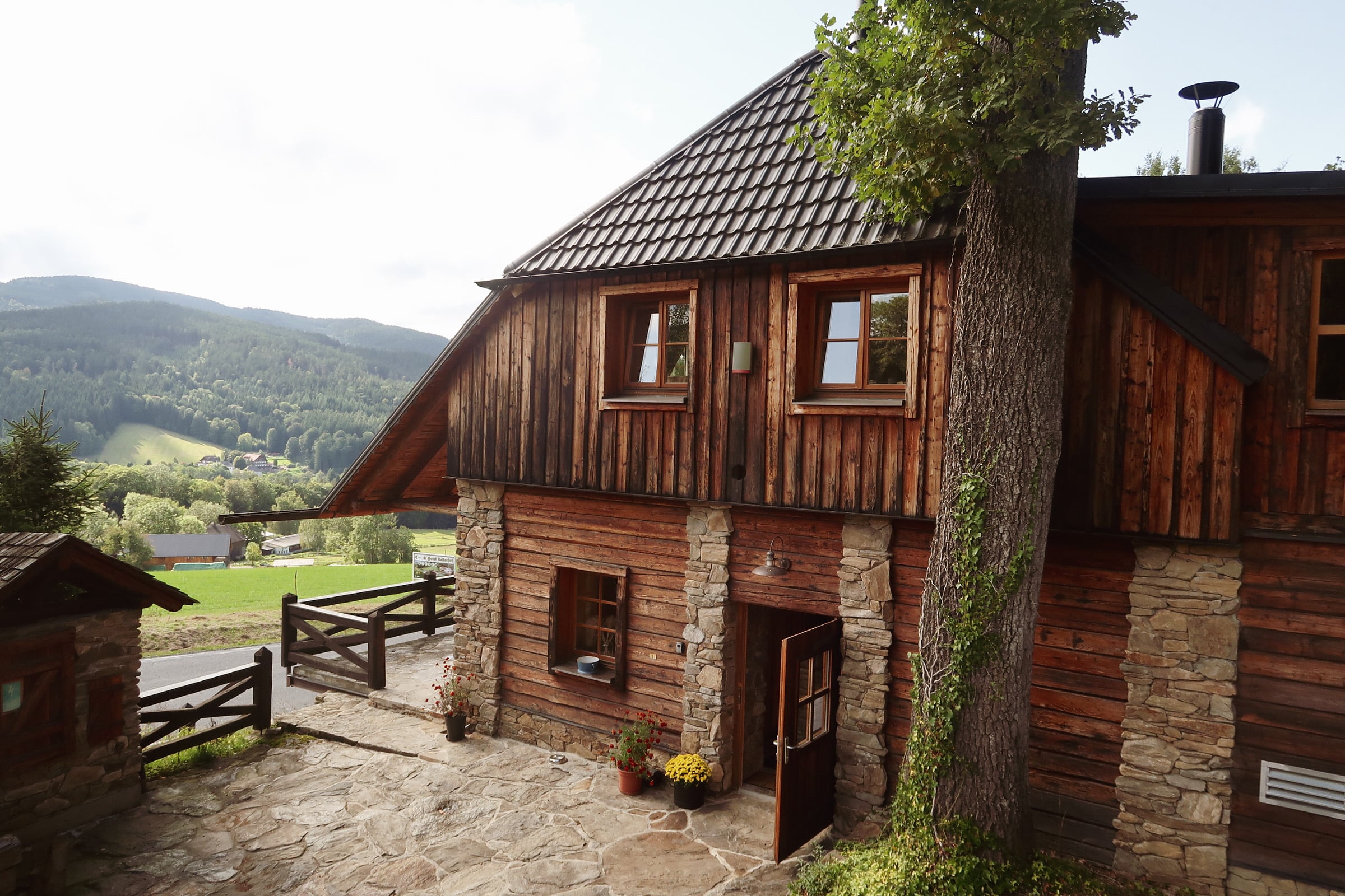Das Blockhaus von Penzion Berry mit Steinpfeilern und gepflasterter Terrasse, im Hintergrund ein bewaldetes Tal
