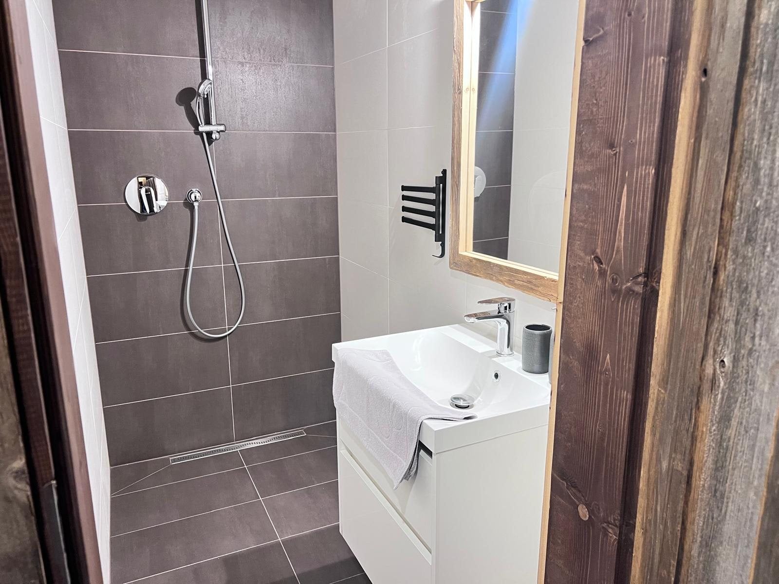 Bathroom with a shower and washbasin next to the log house's wooden panelling