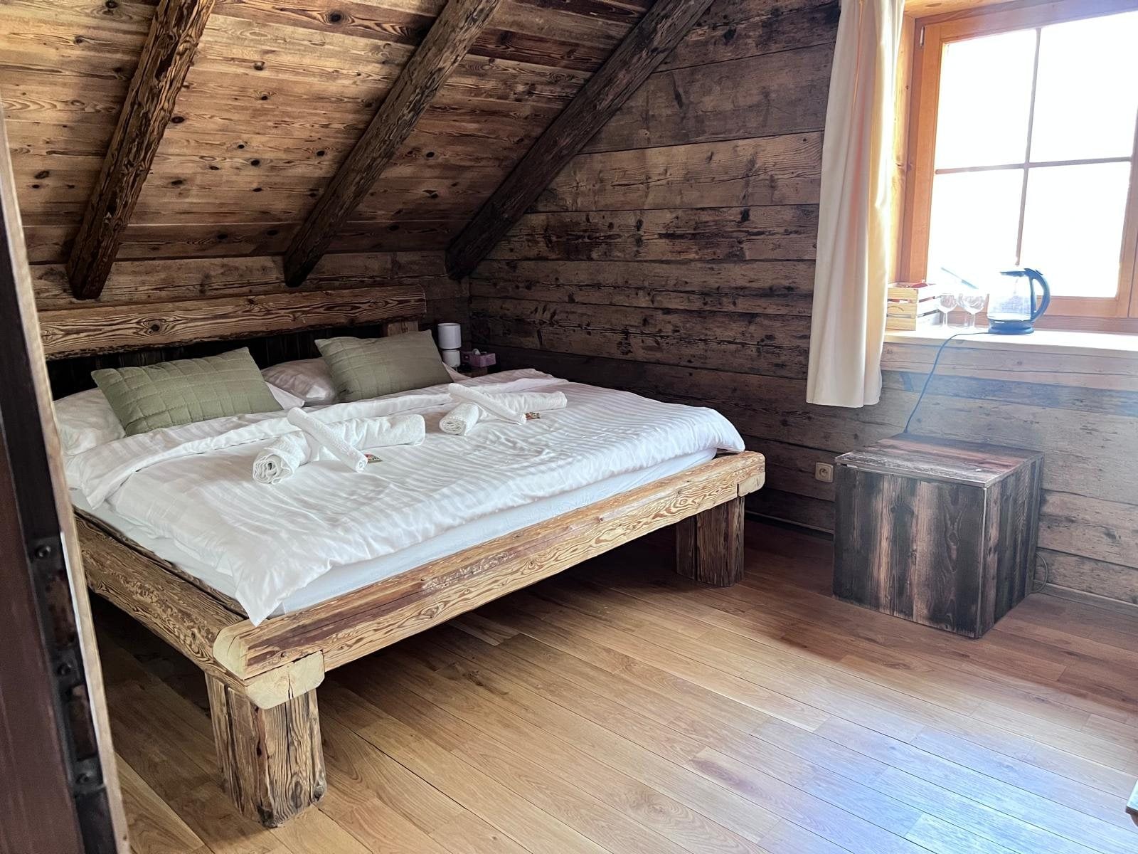 Attic bedroom with a solid wood double bed under the beams and a kettle by the window