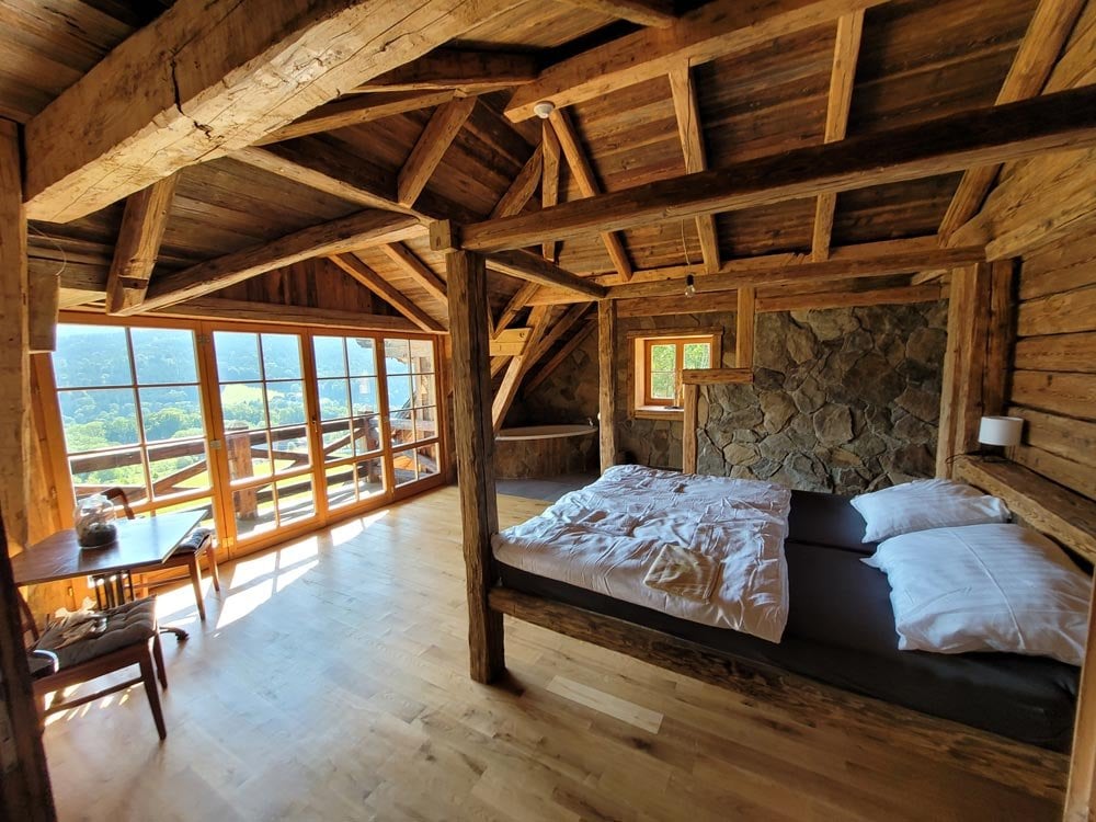 Zimmer Ostrý 1 – Bett mit Holzpfosten, Steinwand und Fenster zu den Bergen