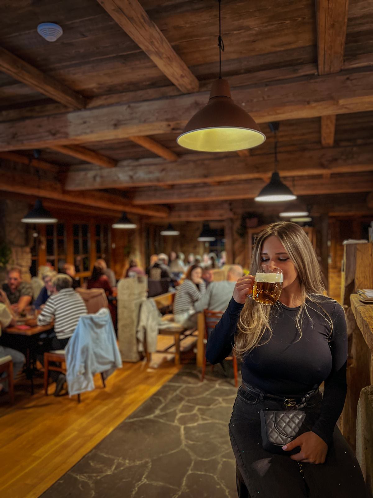 Ein Gast trinkt frisch gezapftes Pilsner im Restaurant unter den Balken, dahinter volle Tische unter Lampen