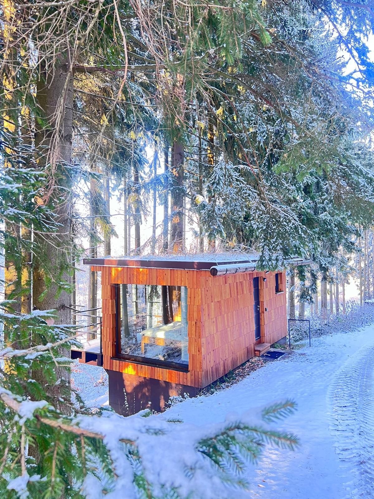 Tiny house mezi zasněženými smrky, prosklenou stěnou svítí světlo